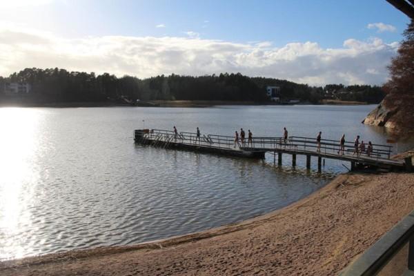 sandstrand med brygga där många går mot vattnet