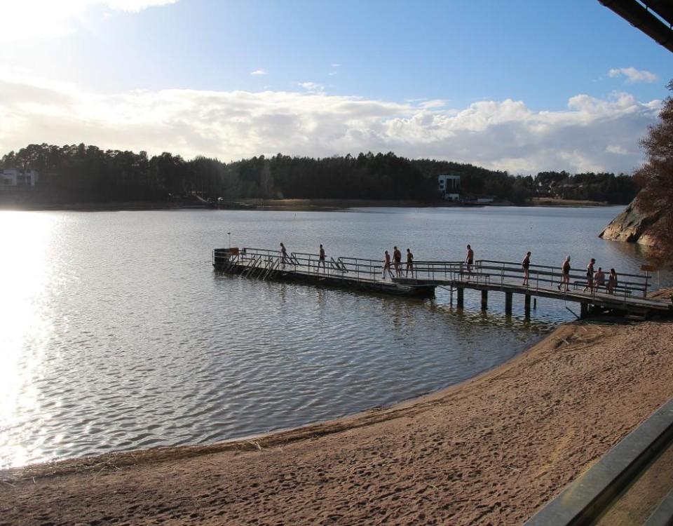 sandstrand med brygga där många går mot vattnet