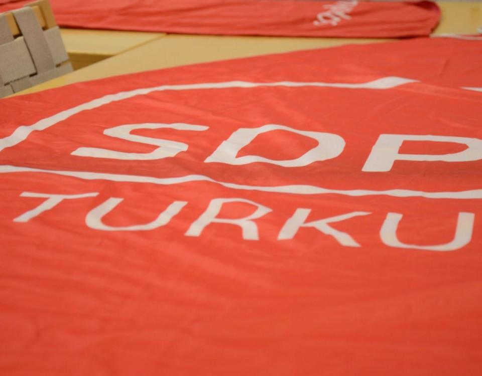 Röd skylt med texten "SDP Turku" ligger på ett bord.