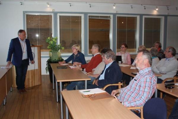 Människor som sitter vid bord i ett konferensrum. Bild tagen från sidan.