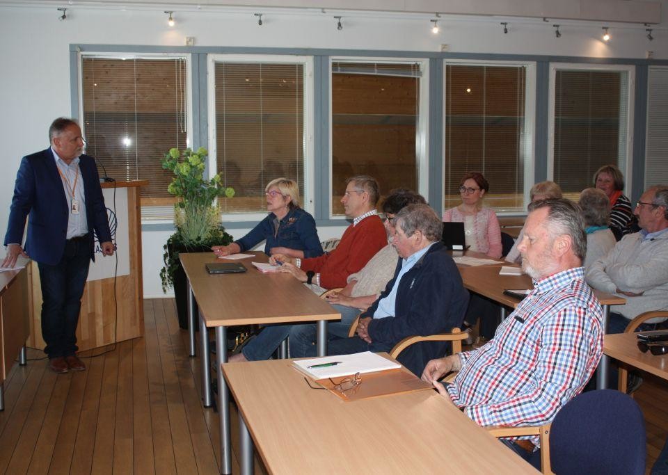 Människor som sitter vid bord i ett konferensrum. Bild tagen från sidan.