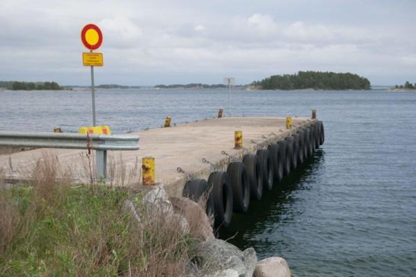 Vikare bryggan i Hitis, trafikmärke på bryggan, vatten, grå himmel och holme i bakgrunden