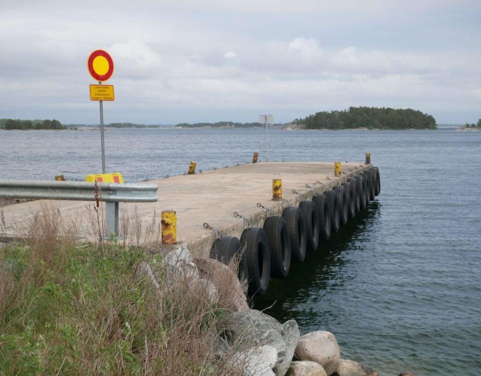 Vikare bryggan i Hitis, trafikmärke på bryggan, vatten, grå himmel och holme i bakgrunden