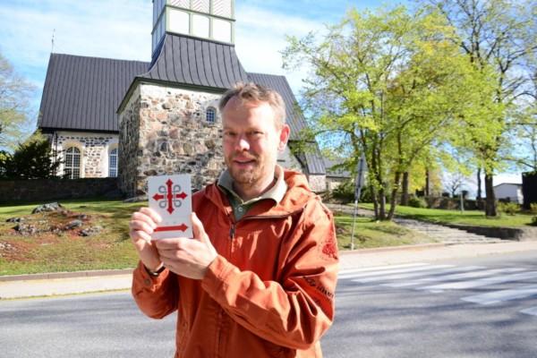 Man står framför Pargas kyrka och håller upp en skylt med pilgrimsmärke