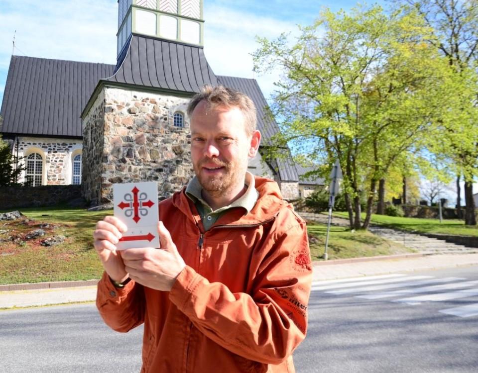 Man står framför Pargas kyrka och håller upp en skylt med pilgrimsmärke