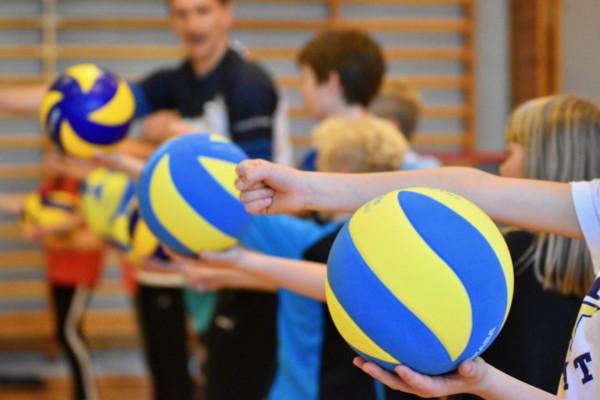 Barn tränar volleyboll i gymnastiksal.