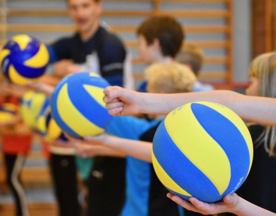 Barn tränar volleyboll i gymnastiksal.