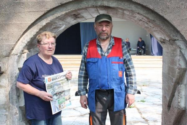 Runa Heino håller i Västanfjärds Bulletin och står bredvid Max Andersson, under en ruinport i sten.