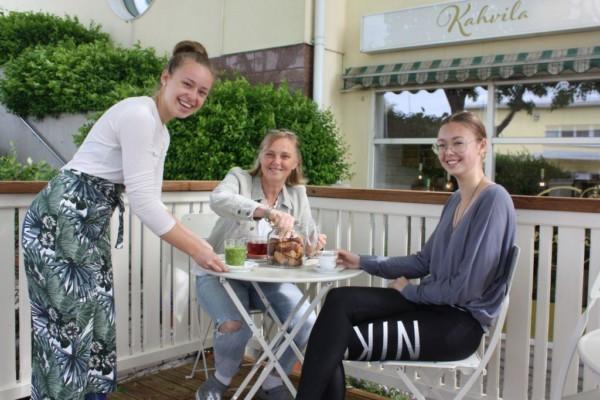 Cecilia, Weckström står bredvid ett vitt runt bord som Nina Björkman och Wilma Weckström sitter vid, i bakgrunden en byggnad och gröna buskar