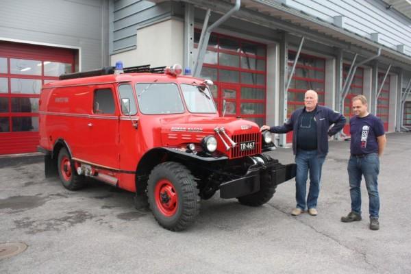 Röd brandbil från 1940-talet, bredvid står Per Sundström och Hasse Korsström, Kimito brandstation i bakgrunden