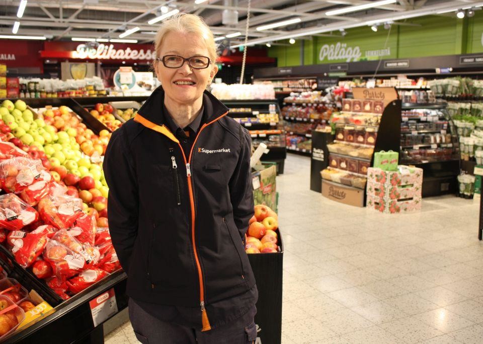 Anne Nyman står vid frukt- och grönskaksavdelningen i K-Supermarket, bredvid äpplena.