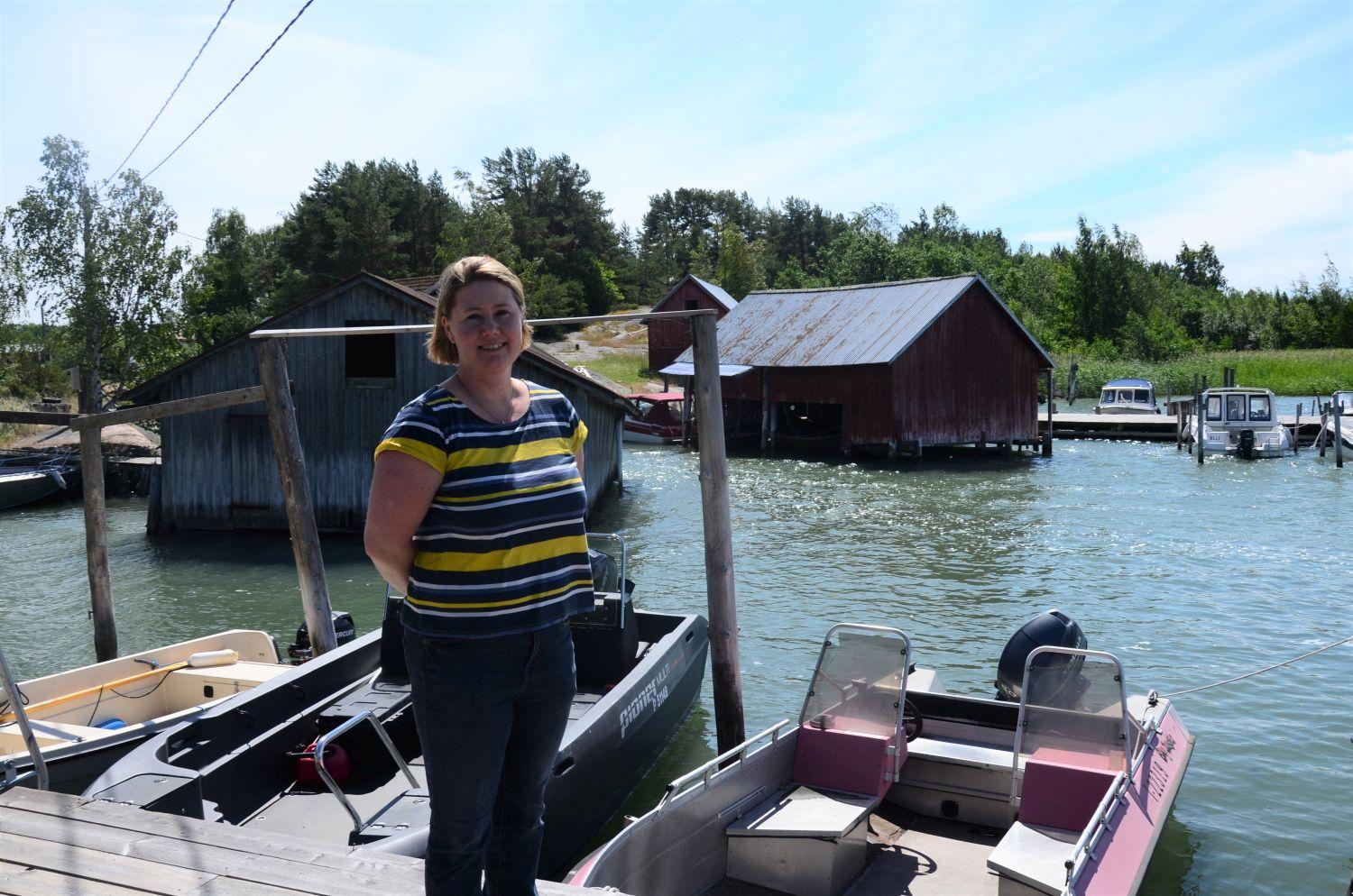 Tiina Pöyli på Jumo bystrand. I bakgrunden syns trähus och båtar vid bryggorna.