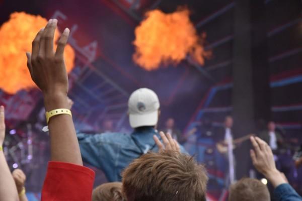 en man sitter pånågon axlar i publiken på en konsert. På scenen ser man pyroteknik