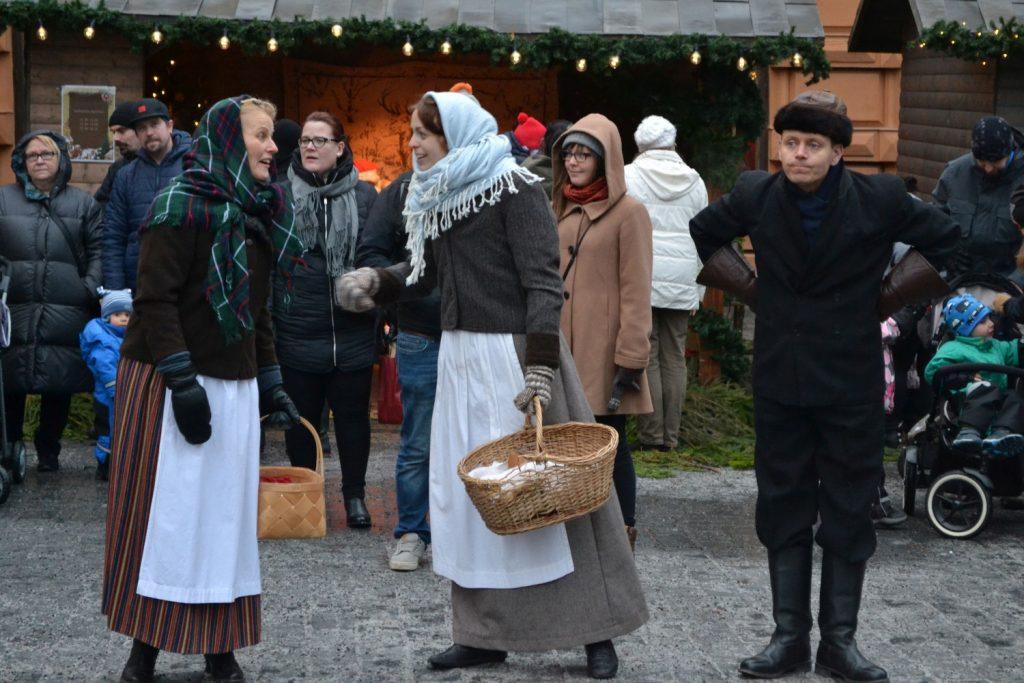 Tre personer i gammaldags kläder på torget