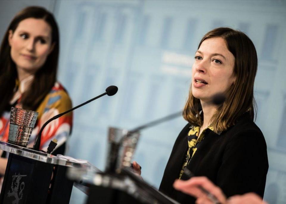 Två kvinnor står och talar i mikrofoner på en presskonferens.