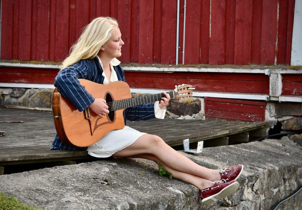 Ung ljushårig kvinna sitter på en klippa med en gitarr i famnen.