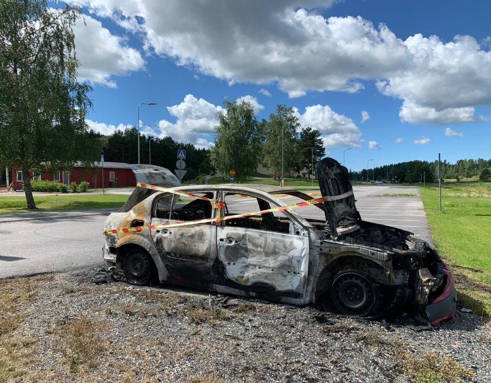 En brunnen bil inlindad i varningstejp på en annars tom parkeringsplats.