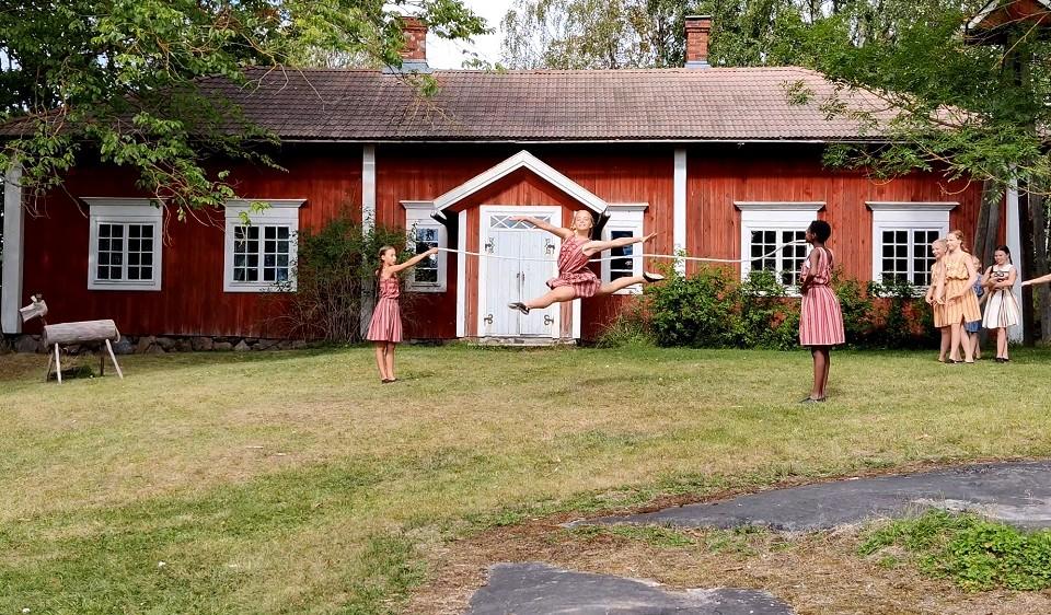 Flickor dansar på gräsmattan framför gammalt hus