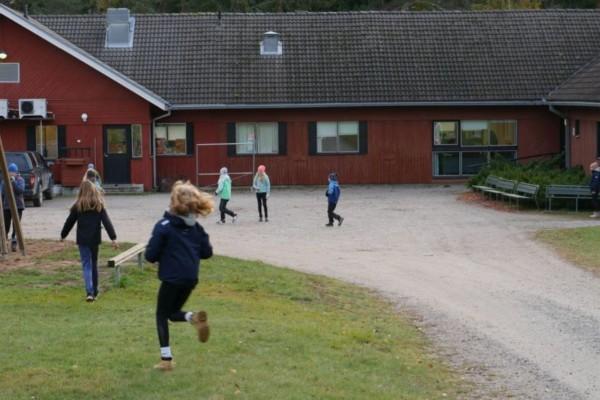 skolelever springer utanför ett rött skolhus