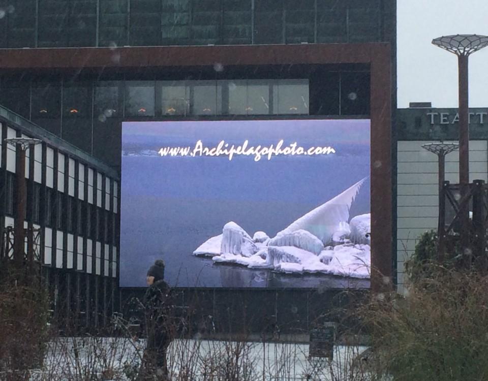 skärm på husvägg, på skärmen syns havsband vintertid