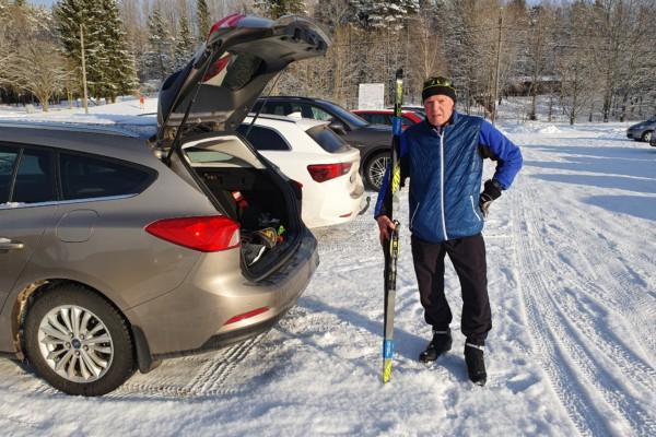 Arto Aunola står vid den öppna bakluckan på sin bil och håller i ett par skidor.