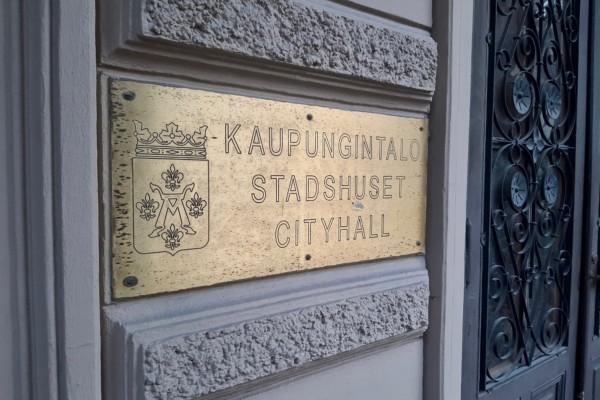 mässingsskylt med text och stadsvapen på husvägg