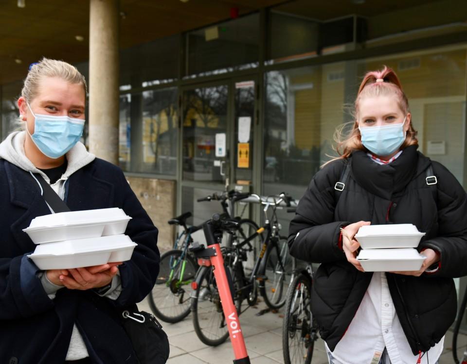 två kvinnor med munskydd står med hämtmatslådor i sina händer