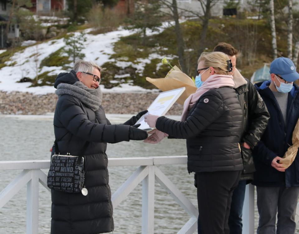 kvinna tar emot pris o tavla, står utomhus