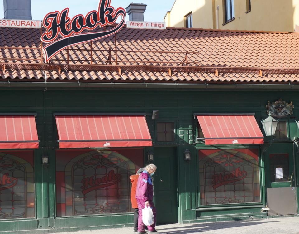 två äldre personer med munskydd går förbi en stängd restaurang