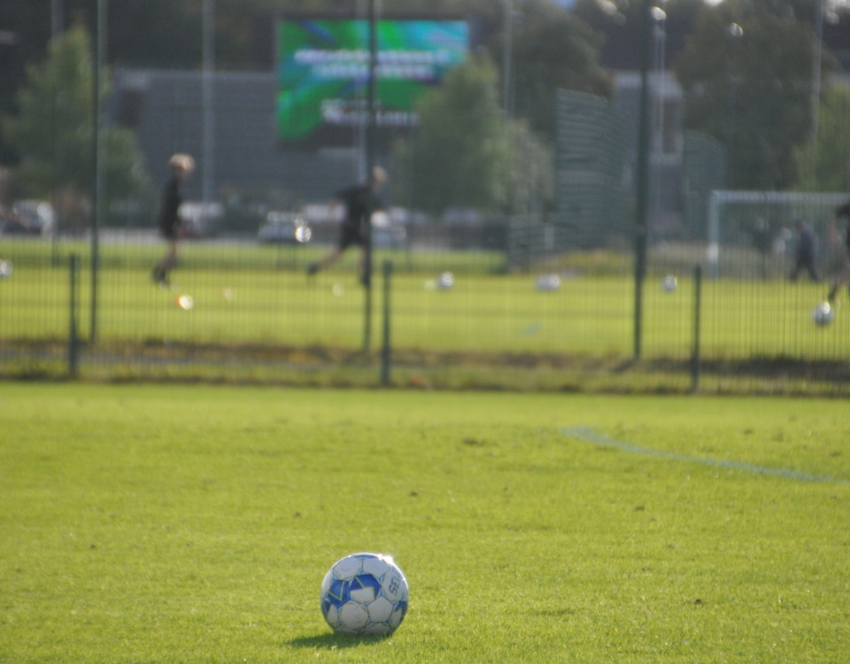 en fotboll ligger på fotbollsplan, i bakgrunden skymtar flera fotbollsspelare