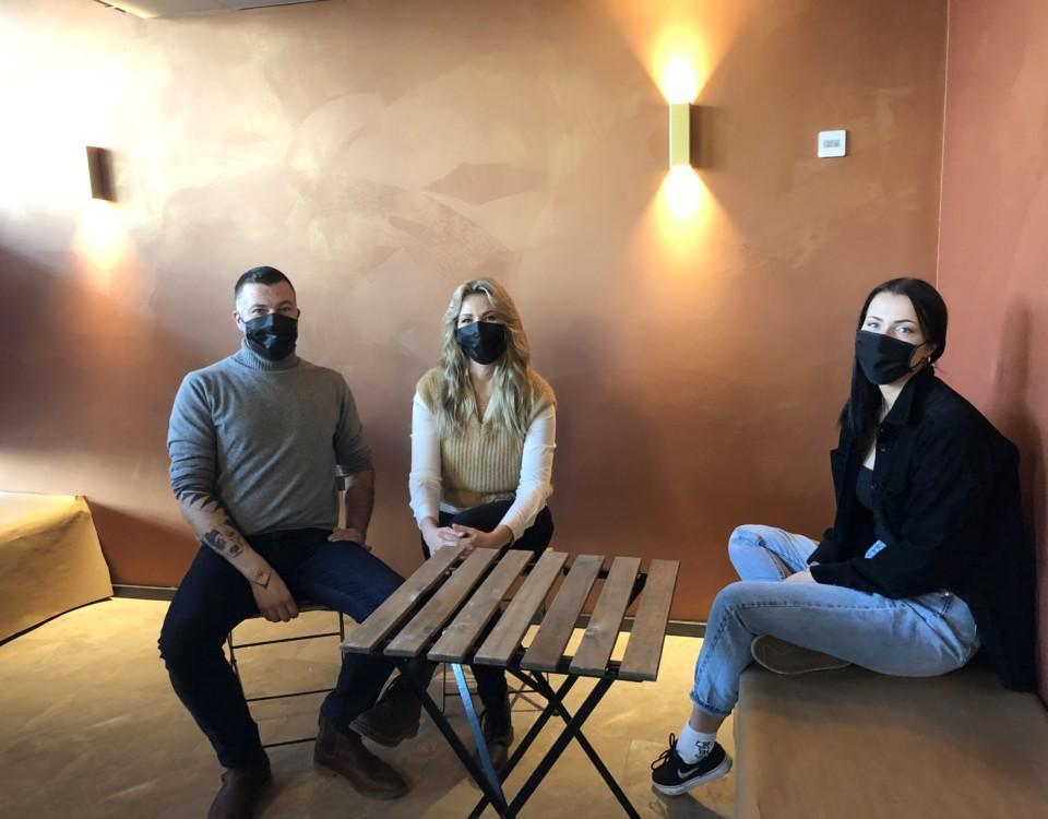 en man och två kvinnor med munskydd sitter vid ett bord