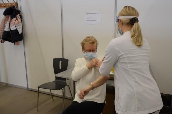 kvinna sitter på en stol och sköterska putsar hennes arm för vaccin