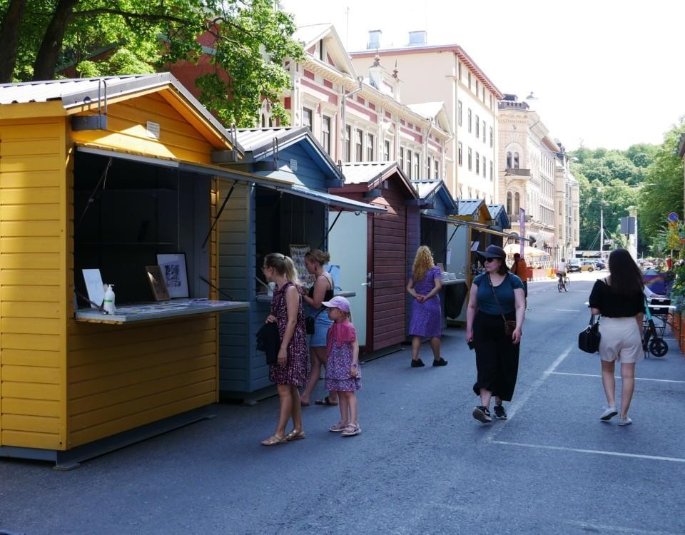 En rad med färgglada försäljningsstånd och människor som strosar runt på en sommargata.