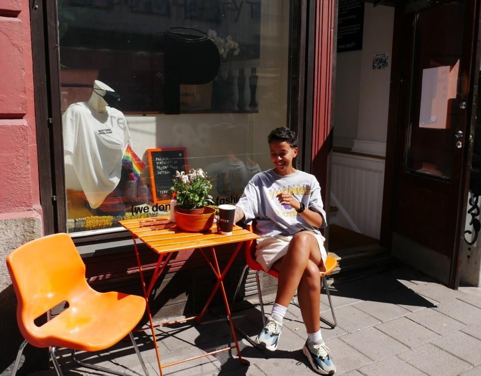 En ung kvinna sitter i solskenet utanför en second hand-affär.