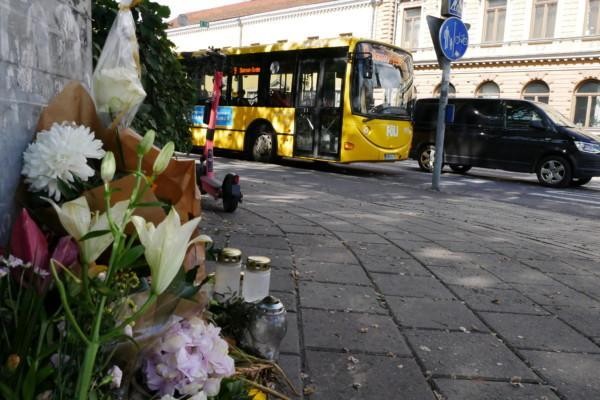 blommor och ljus på en trattoar, buss och parkerad elsparkcykel i bakgrunden