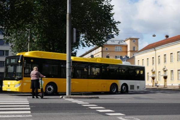 en buss gör en sväng och en person med elsparkcykel väntar på att gå över vägen