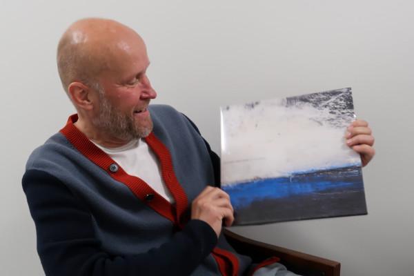 Porträtt av man som sitter och håller upp en vinylalbum som han tittar på. Albumets omslag föreställer en målning av ett hav.