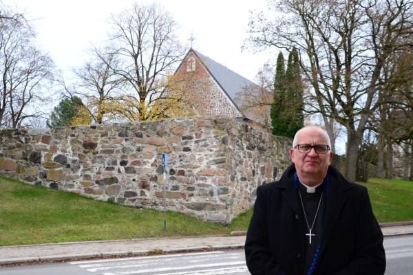 en manlig präst står framför en kyrka