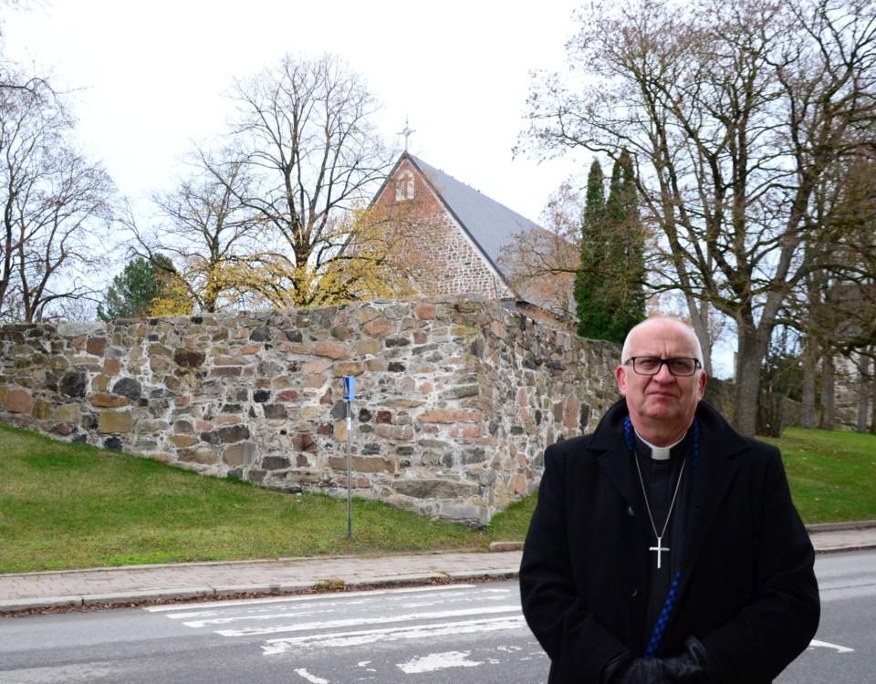 en manlig präst står framför en kyrka