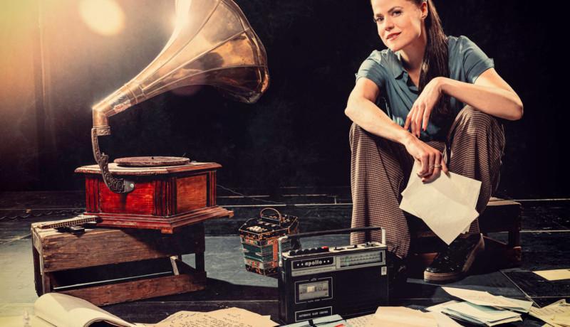 Kvinna sitter bland apparater som gammal grammofon och radio.