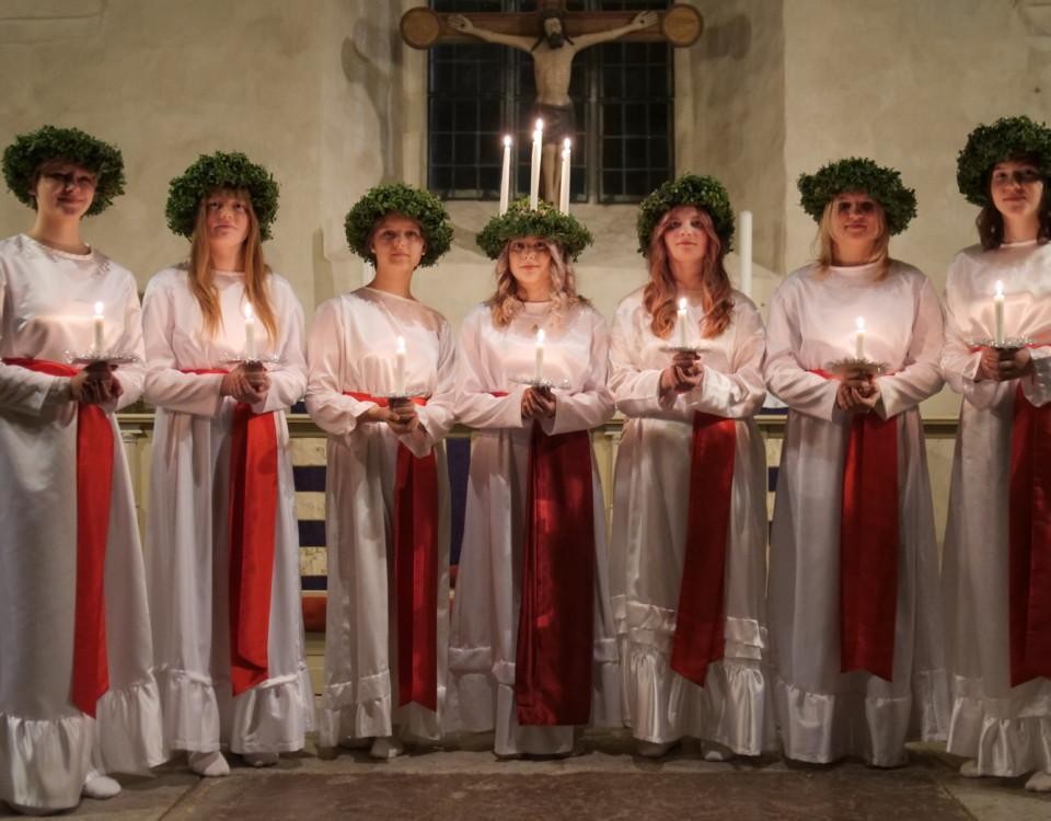 Lucia med ljus i håret och tärnor med kransar på huvudena.