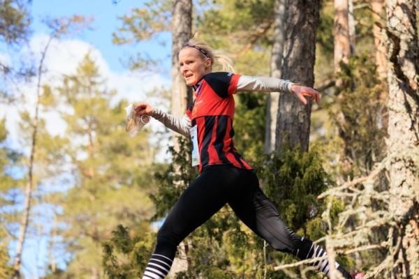 En kvinna iklädd orienteringsdräkt springer i skogen.
