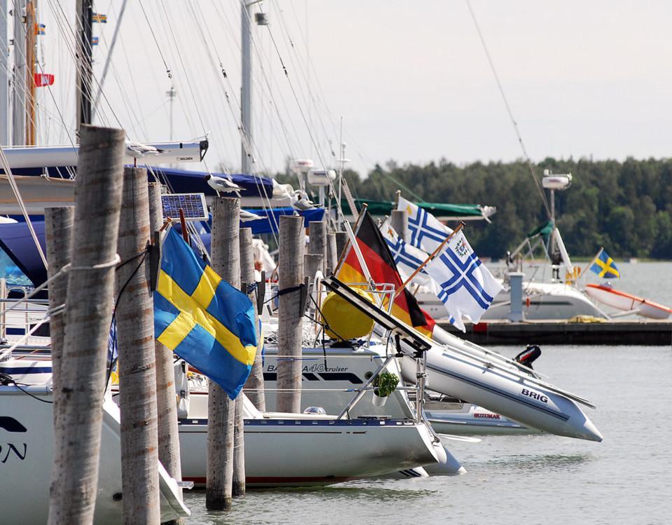 Båtar med olika flaggor i aktern i en gästhamn.