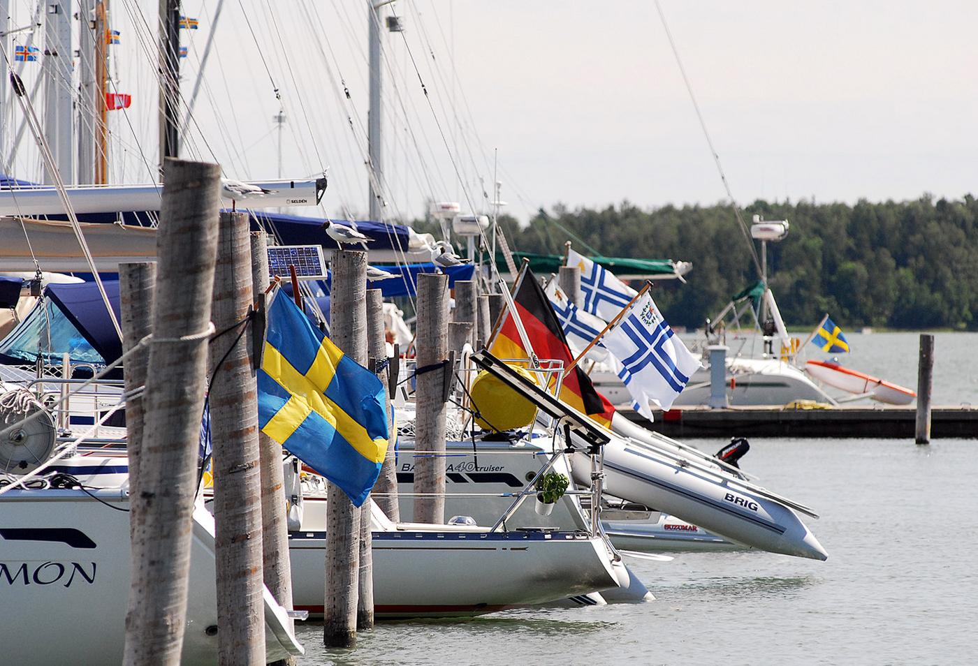 Båtar med olika flaggor i aktern i en gästhamn.