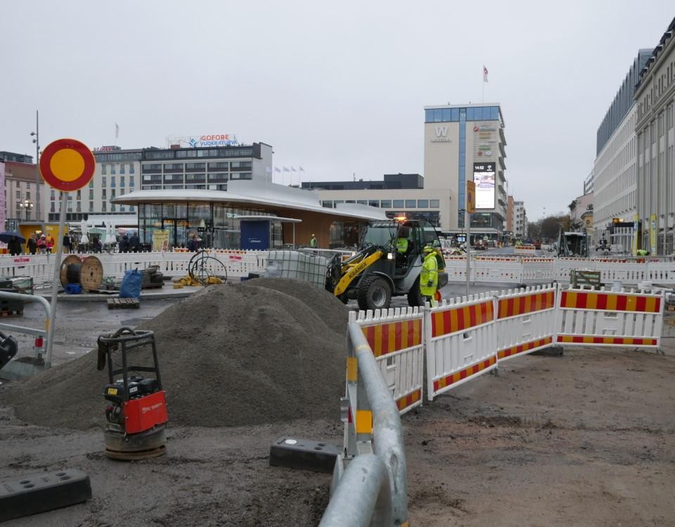 Kaos med arbetsfordon, staket, grushögar och reflexvästklädda arbetare på Salutorget i Åbo.