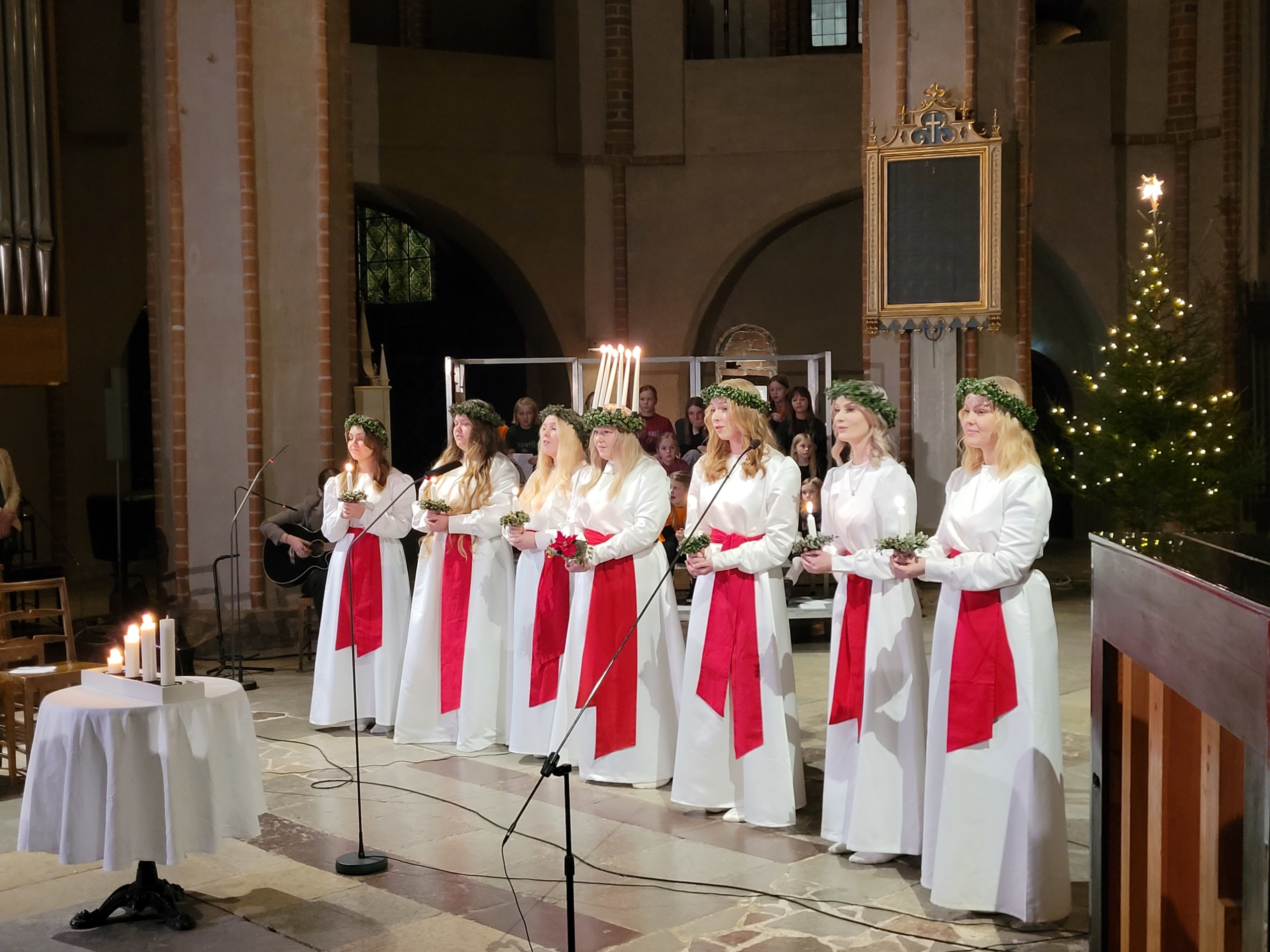 Ett luciafölje står på rad i en kyrka.