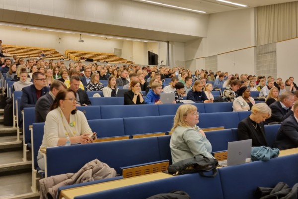 massor av människor i stort auditorium med blå stolar