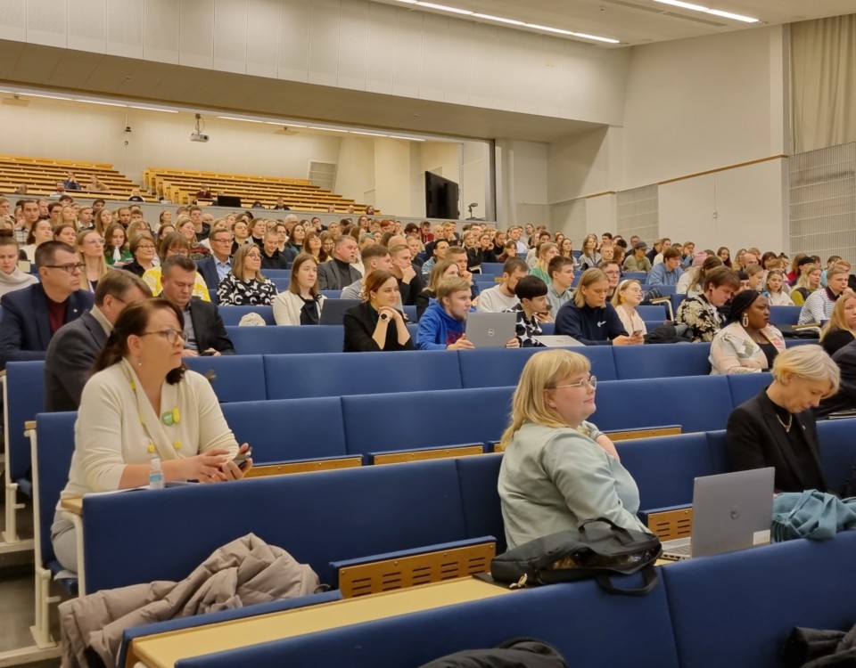 massor av människor i stort auditorium med blå stolar