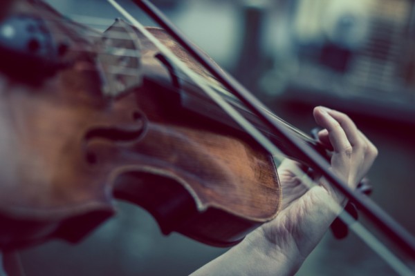 En violin, en stråke och en hand som spelar på instrumentet