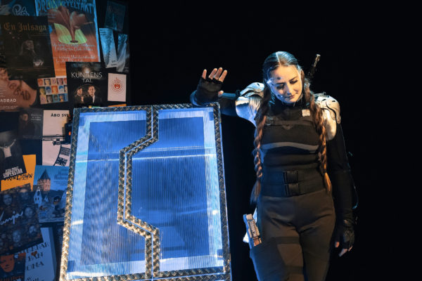 Kvinna med långa flätor står bredvid futuristisk blåskimrande låda i plast och metall.